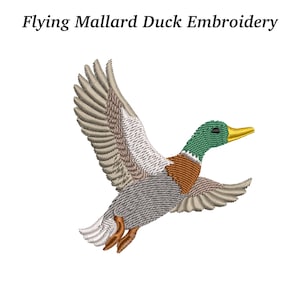May include: An embroidered image of a flying mallard duck with outstretched wings. The duck features a green head, brown chest, gray body, and tan wings. The text "Flying Mallard Duck Embroidery" is above the image.