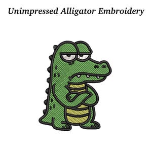 May include: An embroidered design featuring a green alligator with black outlines and a yellow belly. The alligator has a grumpy expression with crossed arms. The text "Unimpressed Alligator Embroidery" is above the alligator.