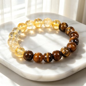 Puede incluir: Una pulsera de cuentas con una disposición circular de cuentas esféricas pulidas. Una mitad de la pulsera consta de cuentas de citrino amarillo translúcido, mientras que la otra mitad está compuesta por cuentas de ojo de tigre marrón opaco con bandas oscuras.