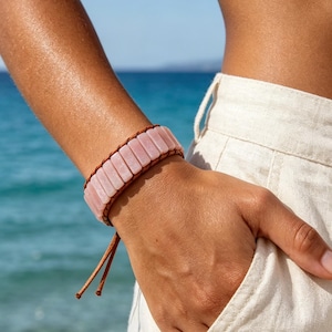 Peut inclure: Un bracelet composé de perles rectangulaires en pierre rose clair disposées en une seule rangée. Les perles sont maintenues par un cordon marron qui les entoure et se termine par deux fines attaches pendantes au bas du bracelet.