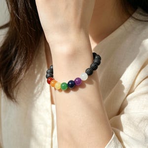 May include: A beaded bracelet featuring a combination of black lava rock beads and colorful chakra stones. The bracelet showcases a spectrum of colors, including red, orange, yellow, green, blue, purple, and white, creating a vibrant and balanced design.