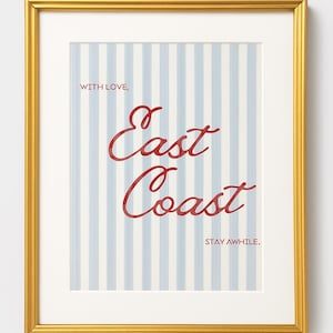 May include: Gold framed art print. The artwork has a striped background in light blue and white, with the words "East Coast" in red script. The text "Stay Awhile" is also included.