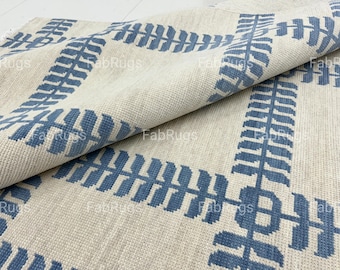 May include: Beige and blue patterned rug. The rug features a repeating geometric design in blue against a neutral beige background. The design includes leaf-like shapes and rectangular borders. The rug is folded over, showing the texture and pattern.