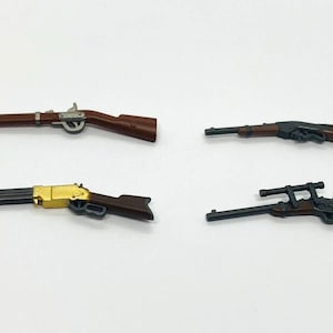 Puede incluir: Cuatro rifles de juguete en miniatura de varios diseños. Los rifles son principalmente marrones y negros, con algunos detalles plateados y dorados. Los rifles están dispuestos sobre una superficie blanca.