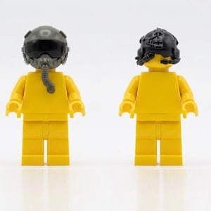 Puede incluir: Dos figuras Lego amarillas, una con un casco de piloto gris y un aparato respiratorio, la otra con un casco negro. Las figuras están de pie sobre un fondo blanco. Una divertida interpretación de la aviación.