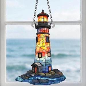 Puede incluir: Un faro de vidrieras con un diseño colorido, suspendido por una cadena. El faro presenta una parte superior roja y naranja, una sección media negra y un cuerpo con tonos amarillos, naranjas y azules. Se asienta sobre una base rocosa con agua azul.