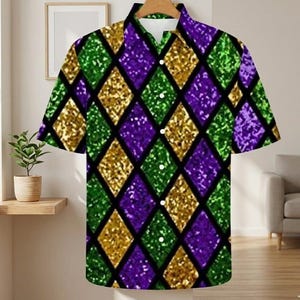 May include: Short-sleeved button-down shirt with a vibrant diamond pattern in gold, green, and purple glitter. The shirt has a classic collar and a relaxed fit, perfect for a casual look. The shirt is hung on a wooden hanger.