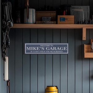 May include: A blue wooden sign with white text that reads "Welcome to Mike's Garage If I can't fix it you're screwed".