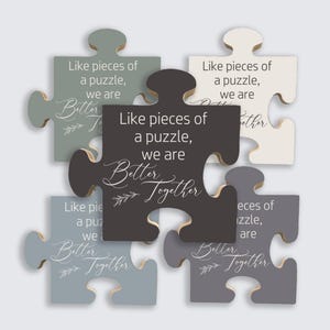 May include: A set of six wooden puzzle pieces in various shades of gray, white, and black. Each piece has the phrase "Like pieces of a puzzle, we are Better Together" printed on it in white script. A decorative item.