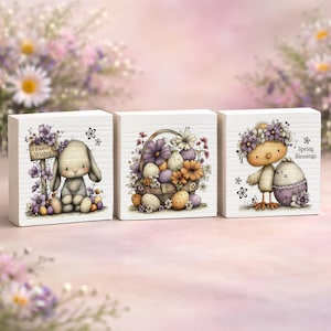 May include: Set of three decorative wooden blocks with Easter-themed illustrations. One block features a bunny with "Easter Wishes" text, another a basket of eggs and flowers, and the last a chick with an egg and "Spring Blessings" text. The blocks are painted with pastel colors.