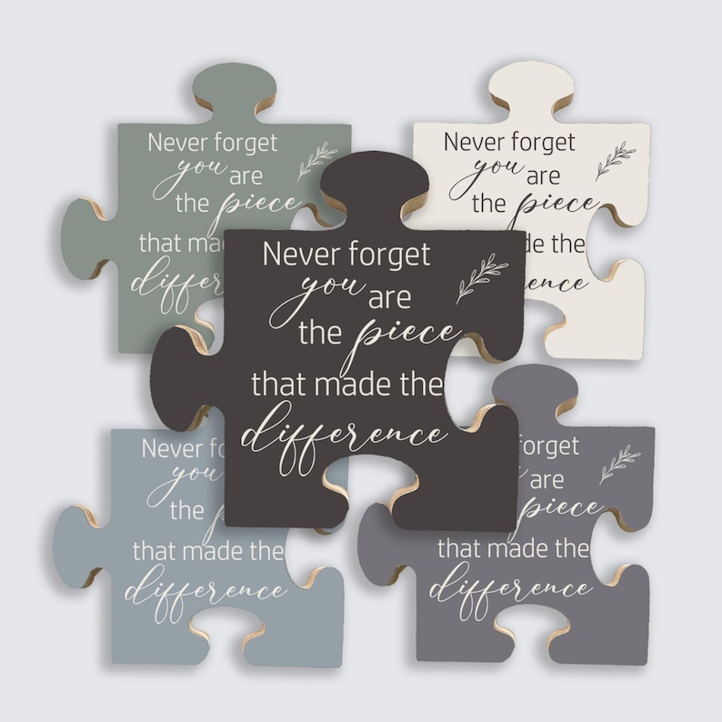 May include: A collection of wooden puzzle pieces in various shades of gray, white, and black. Each piece has the quote "Never forget you are the piece that made the difference" in white script. Decorative sprigs accent the text.