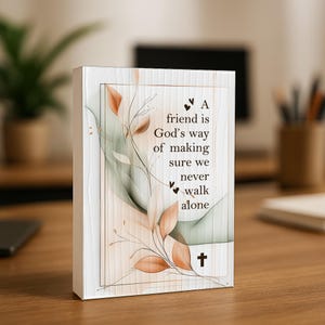 May include: A rectangular canvas print with a white wooden background and a gold border. The print features a quote: "A friend is God's way of making sure we never walk alone." Decorative leaves and a cross are also included.