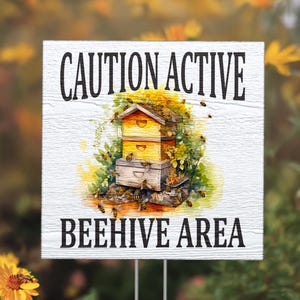 May include: White wooden sign with black text that reads "CAUTION ACTIVE BEEHIVE AREA". The sign features a watercolor illustration of a beehive with bees flying around it.