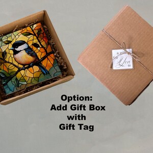 May include: A brown cardboard box with a stained glass style artwork of a bluebird on a branch. The artwork is in a square frame and is surrounded by brown packing paper. The box is open and the artwork is visible. The text "Option: Add Gift Box with Gift Tag" is below the box.