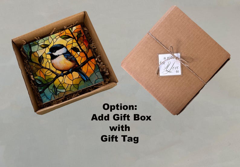 May include: A brown cardboard box with a stained glass style artwork of a bluebird on a branch. The artwork is in a square frame and is surrounded by brown packing paper. The box is open and the artwork is visible. The text "Option: Add Gift Box with Gift Tag" is below the box.