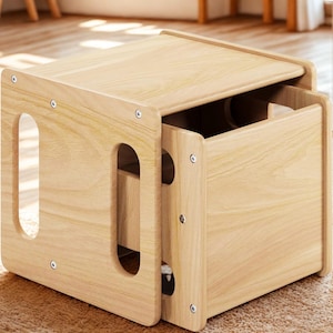 May include: A light-colored wooden nesting table set. The set includes two rectangular tables, one slightly smaller than the other, designed to fit inside each other. Each table has rounded corners and cut-out handles.