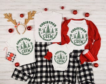 May include: A festive Christmas ensemble featuring white t-shirts, a babygrow, and black and white checked pyjama bottoms. The items display a green graphic with the text "Christmas Crew Making Memories Together". Red decorations are also present.