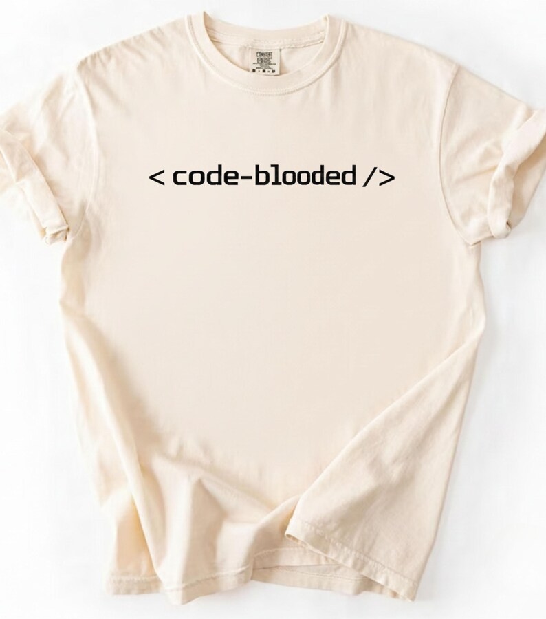 K&ouml;nnte beinhalten: Cremefarbenes T-Shirt mit dem Text "< code-blooded />" in Schwarz. Das Shirt hat einen Rundhalsausschnitt und kurze &Auml;rmel, wobei die &Auml;rmel hochgekrempelt sind. Der Stoff wirkt weich und bequem.