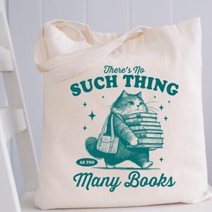 Peut inclure: Sac fourre-tout cr&egrave;me avec une illustration turquoise d'un chat portant des livres. Le texte sur le sac dit "There's No Such Thing As Too Many Books". Le sac est rectangulaire avec deux anses.