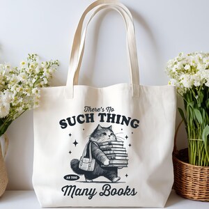 Peut inclure: Sac fourre-tout cr&egrave;me avec une illustration en noir et blanc d'un chat portant une pile de livres. Le texte sur le sac dit : &laquo; Il n'y a pas trop de livres &raquo;.