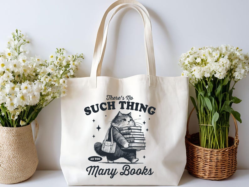 Peut inclure: Sac fourre-tout cr&egrave;me avec une illustration en noir et blanc d'un chat portant une pile de livres. Le texte sur le sac dit : &laquo; Il n'y a pas trop de livres &raquo;.