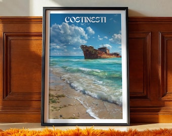 Op de afbeelding: Ingelijste kunstafdruk met een kustscène met een verroest scheepswrak in turquoise water onder een blauwe lucht met wolken. Het woord "COSTINESTI" staat bovenaan gedrukt. De print zit in een zwart frame, rustend op een houten vloer met een oranje tapijt.