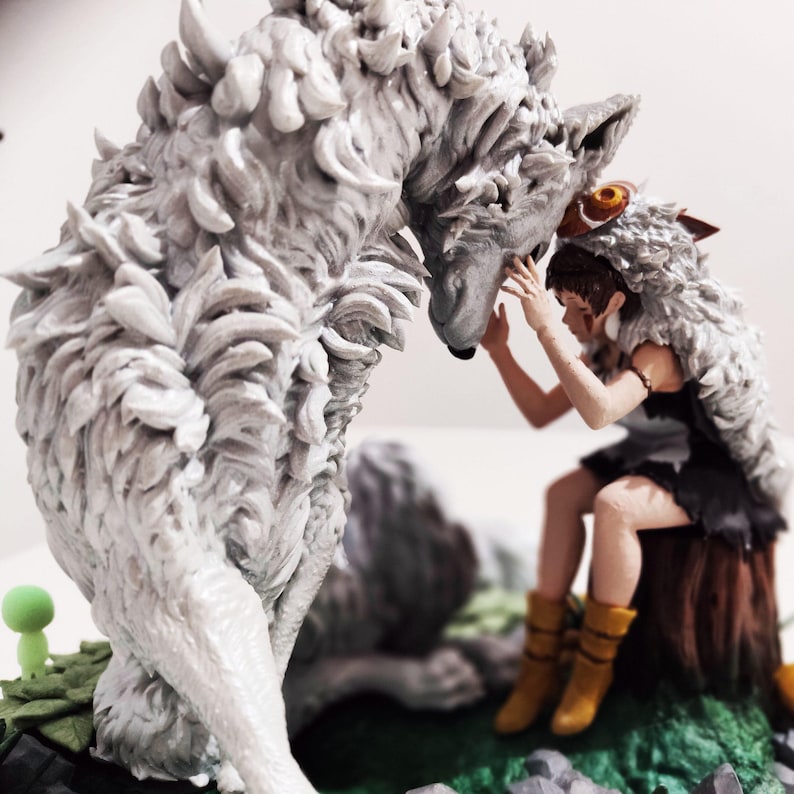 May include: A detailed figurine depicting a wolf and a person. The wolf is large and gray with textured fur. The person is seated, wearing a fur-trimmed hood and a black dress. The scene is set on a base with green and gray elements.