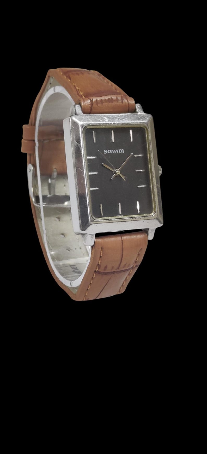Puede incluir: Un reloj Sonata rectangular con esfera negra y marco plateado. El reloj tiene una correa de cuero marr&oacute;n. La esfera del reloj tiene marcadores y manecillas blancas. La palabra "SONATA" est&aacute; impresa en la esfera.
