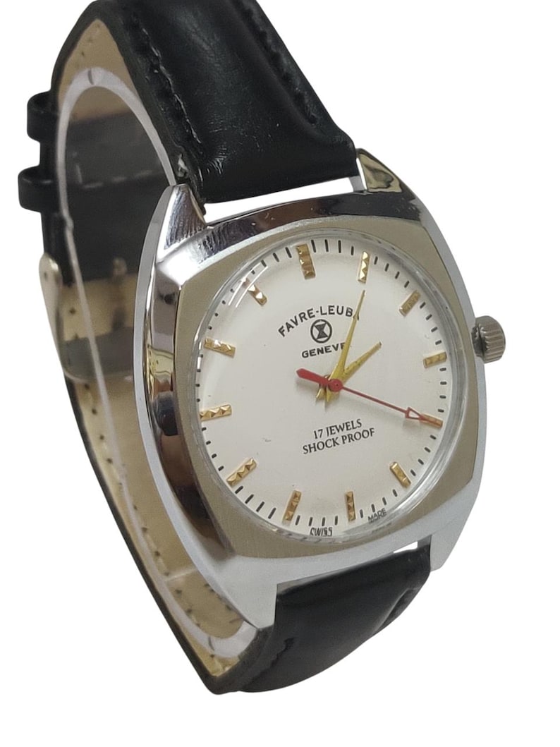 May include: A silver Favre-Leuba Geneve wristwatch with a white face, gold markers, and a black leather strap. The watch face displays "17 Jewels Shock Proof" and "Swiss Made". The watch has a red second hand.