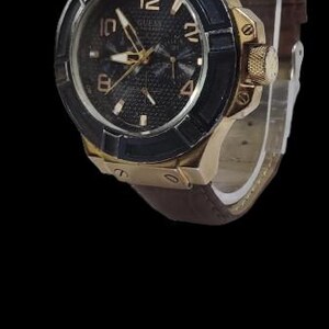 Peut inclure: Une montre Guess dor&eacute;e avec un cadran noir et un bracelet en cuir marron. La montre pr&eacute;sente des aiguilles et des index dor&eacute;s, avec une lunette noire. Le cadran est textur&eacute; et le bracelet est en cuir marron.