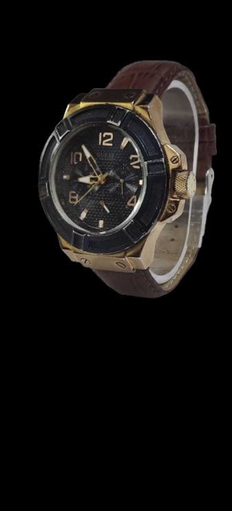 Peut inclure: Une montre Guess dor&eacute;e avec un cadran noir et un bracelet en cuir marron. La montre pr&eacute;sente des aiguilles et des index dor&eacute;s, avec une lunette noire. Le cadran est textur&eacute; et le bracelet est en cuir marron.