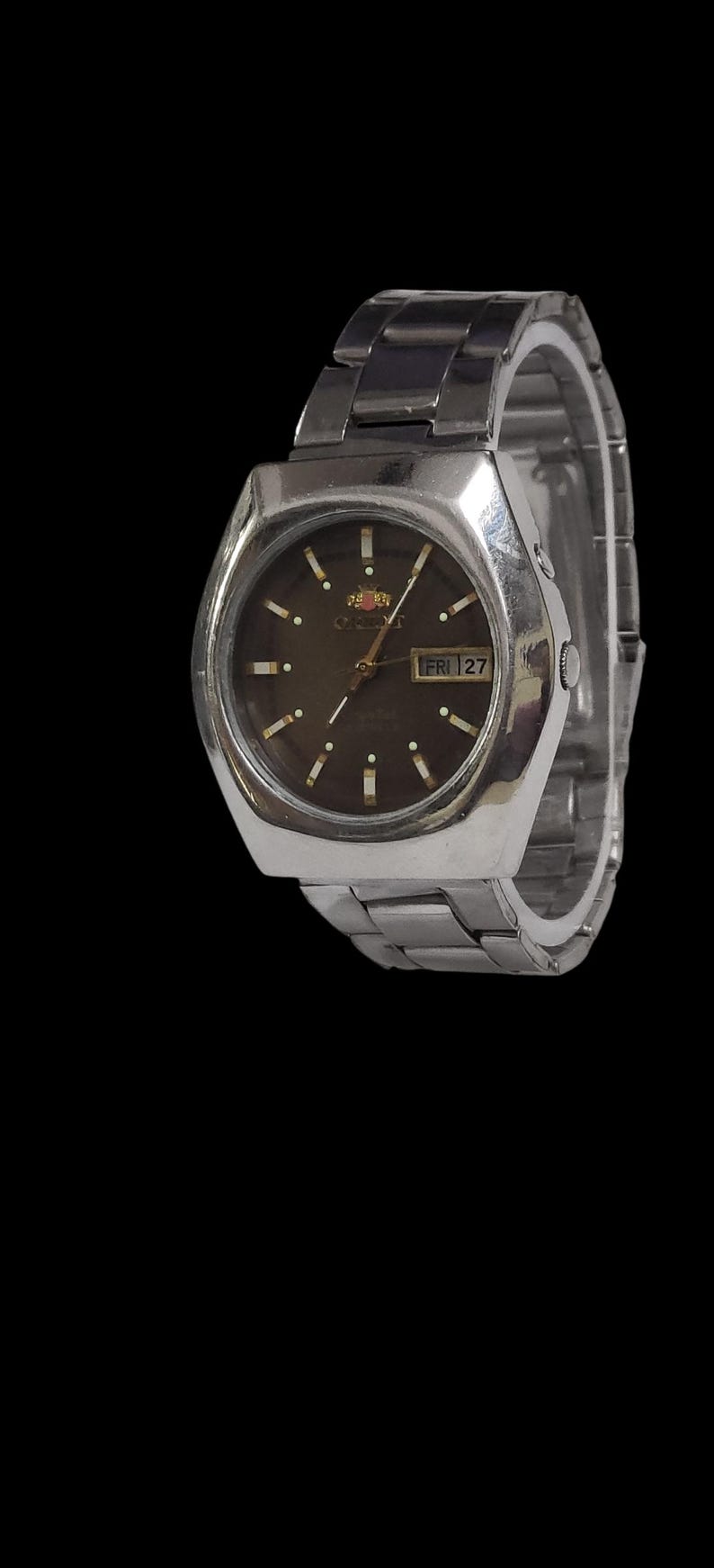 K&ouml;nnte beinhalten: Eine silberfarbene Orient-Uhr mit dunkelbraunem Zifferblatt und Metallarmband. Das Zifferblatt zeigt den Tag und das Datum an. Die Uhr hat ein rechteckiges Geh&auml;use und ein silberfarbenes Metallarmband.