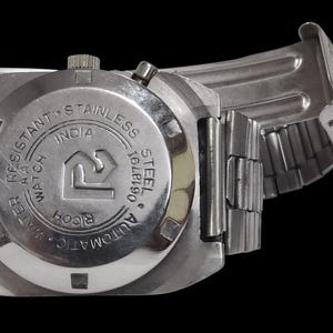 Pu&ograve; includere: Un orologio da polso in acciaio inossidabile con cinturino in metallo argentato. Il quadrante dell'orologio &egrave; visibile, con la scritta "WATER RESISTANT", "STAINLESS STEEL" e "INDIA". L'orologio &egrave; un modello automatico.