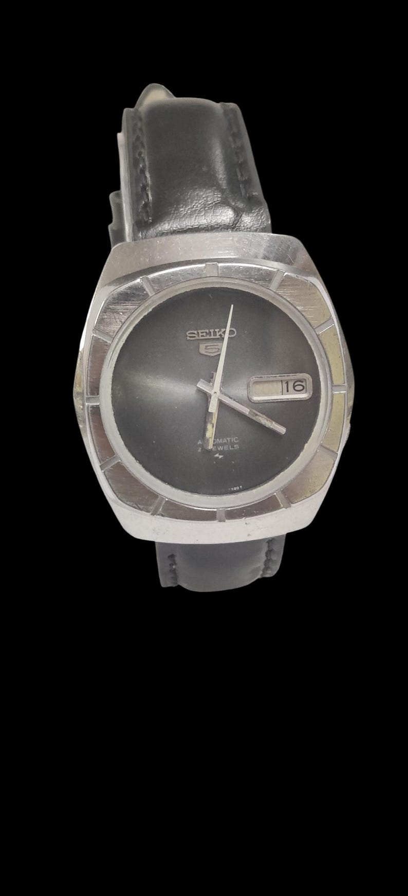May include: A vintage Seiko watch with a black dial and silver-tone case. The watch features a date display at the 3 o'clock position and a black leather strap. The watch face has the word "SEIKO" and "AUTOMATIC 2 JEWELS" printed on it.