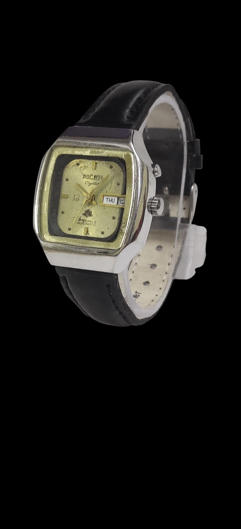 May include: A vintage wristwatch with a silver case and a gold-coloured face. The watch has a black leather strap and shows the day and date. The watch face has the brand name "Michel" and the word "Crystal" printed on it.