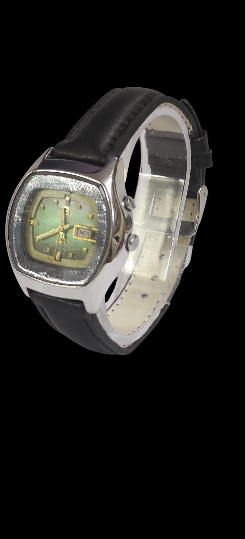 Puede incluir: Un reloj de pulsera vintage con una caja rectangular plateada y una esfera verde. El reloj presenta agujas e indicadores dorados, y una pantalla de d&iacute;a y fecha. Tiene una correa de cuero negro.
