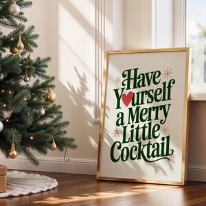 May include: A framed print with the text "Have Yourself a Merry Little Cocktail" in green and white, with a red heart. The print is in a gold frame and leans against a wall next to a decorated Christmas tree.