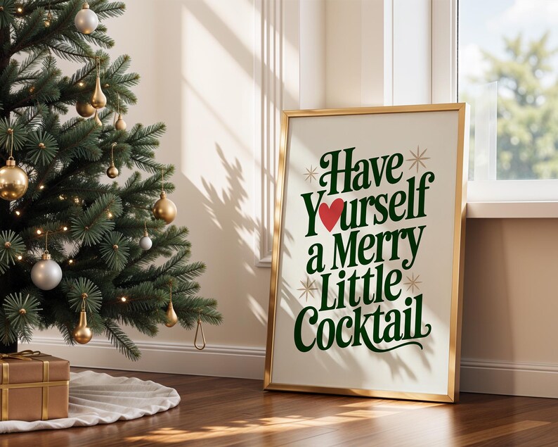 May include: A framed print with the text "Have Yourself a Merry Little Cocktail" in green and white, with a red heart. The print is in a gold frame and leans against a wall next to a decorated Christmas tree.