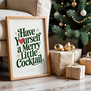 May include: A framed print with the text "Have Yourself a Merry Little Cocktail" in green and red. The print is propped against a beige sofa and a Christmas tree with wrapped gifts.