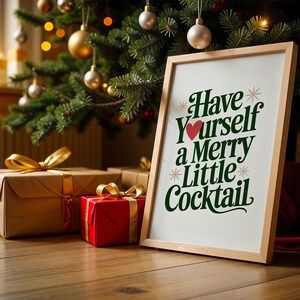 May include: A framed print with the text "Have Yourself a Merry Little Cocktail" in green and red, resting on a wooden floor. The print is next to wrapped gifts with gold ribbons, under a decorated Christmas tree.