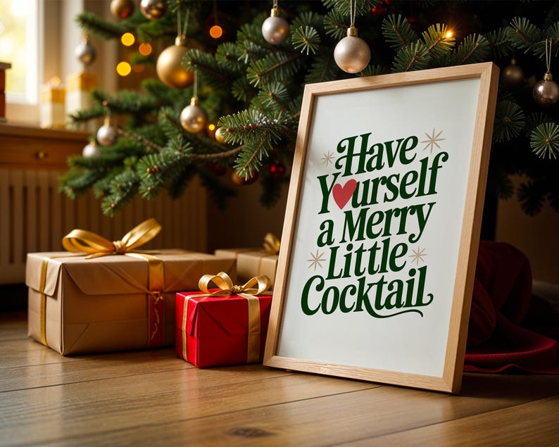 May include: A framed print with the text "Have Yourself a Merry Little Cocktail" in green and red, resting on a wooden floor. The print is next to wrapped gifts with gold ribbons, under a decorated Christmas tree.