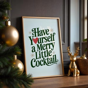 May include: A framed print with the text "Have Yourself a Merry Little Cocktail" in green script and a red heart. A gold-colored deer figurine and a woven basket sit on a wooden surface.