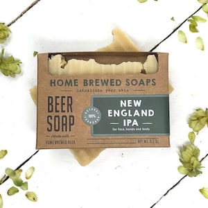 May include: A brown cardboard box with a white bar of soap inside. The box has the text "Home Brewed Soaps" and "New England IPA" printed on it. The soap is made with home-brewed beer and is 3.5 oz.