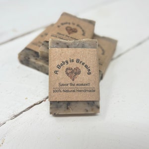 May include: A stack of brown and white soap bars with a label that reads "A Baby is Brewing, Savor the moment! 100% Natural Handmade".