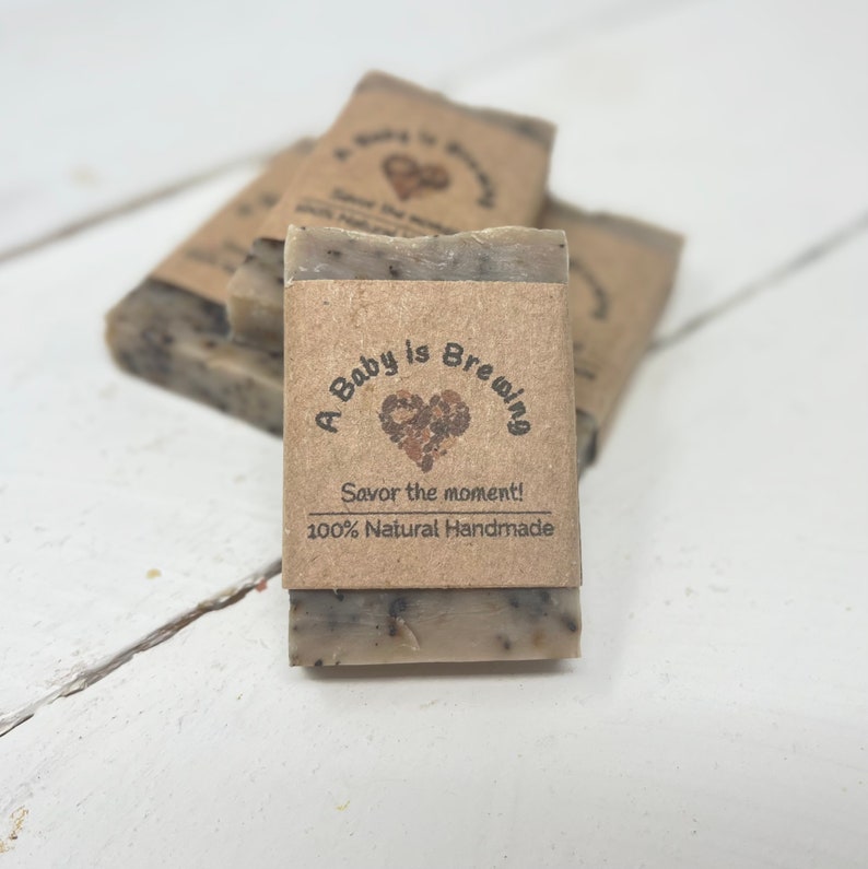 May include: A stack of brown and white soap bars with a label that reads "A Baby is Brewing, Savor the moment! 100% Natural Handmade".