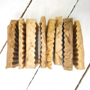 May include: Seven bars of handmade soap with a wavy edge. The bars are a light brown colour and have a natural, rustic look.