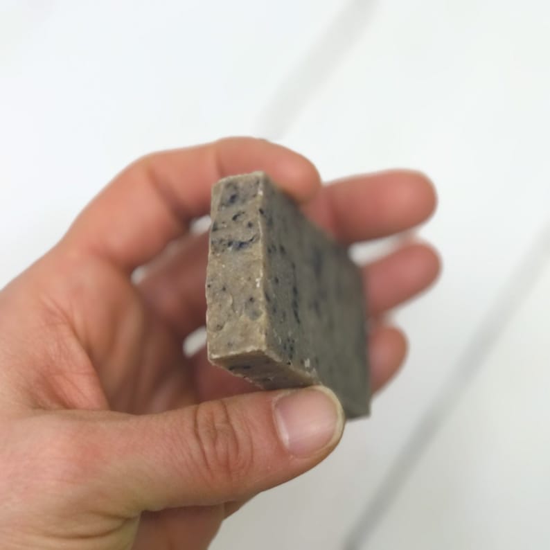 May include: A bar of brown soap with black flecks. The soap is being held in a hand.