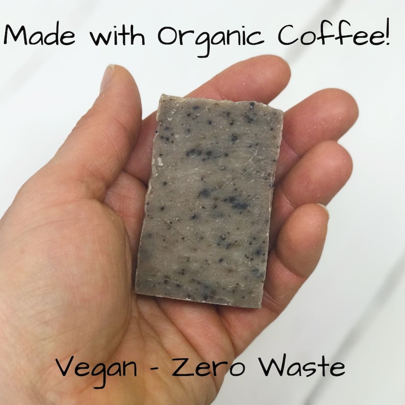 May include: A close-up of a bar of handmade soap with a speckled brown and grey colour. The soap is in a hand and the text "Made with Organic Coffee!" is above the soap. The text "Vegan - Zero Waste" is below the soap.