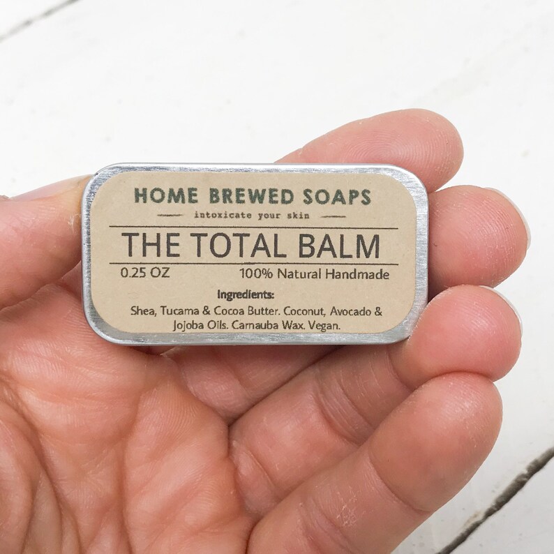Puede incluir: Una peque&ntilde;a lata de plata con una etiqueta marr&oacute;n que dice "HOME BREWED SOAPS intoxicate your skin THE TOTAL BALM 0.25 OZ 100% Natural Handmade Ingredients: Shea, Tucama & Cocoa Butter. Coconut, Avocado & Jojoba Oils. Carnauba Wax. Vegan."