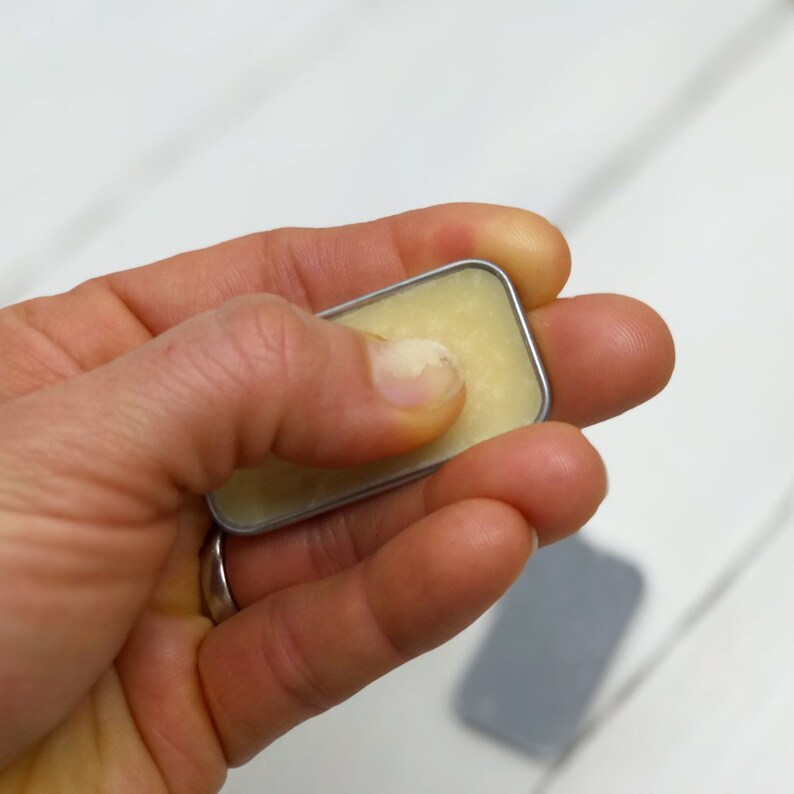 Puede incluir: Una peque&ntilde;a lata plateada con tapa que contiene un b&aacute;lsamo amarillo claro.